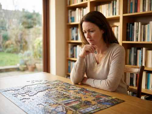 Eine nachdenklich wirkende Frau sitzt in einem Arbeitszimmer und blickt auf ein unvollständiges Puzzle, während sie ein Puzzleteil in der Hand hält. Das Bild symbolisiert die Suche nach fehlenden Verbindungen im Leben, wenn rationales Denken nicht mehr weiterhilft – das Kernthema der systemischen Aufstellung bei Ralf Musto